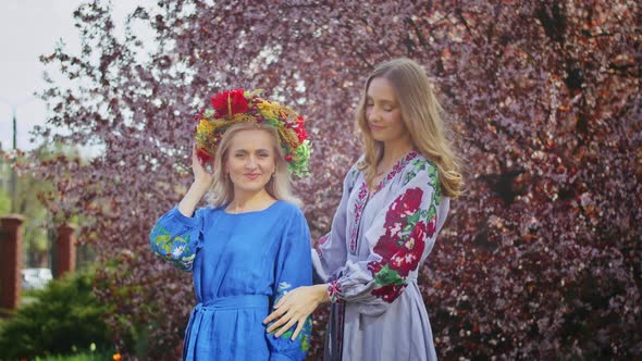 Two Happy Woman in a Wreath on Her Head Rejoices Against the Backdrop of Blooming Pink Sakura alt