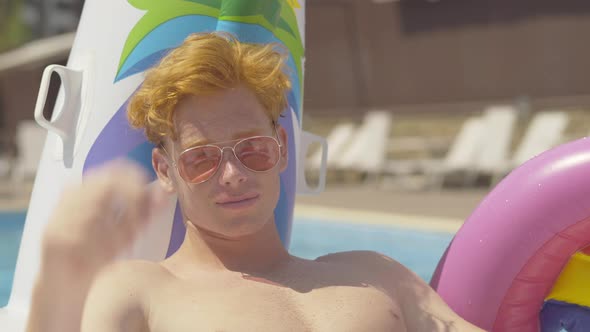 Close-up of Young Handsome Redhead Caucasian Man with Grey Eyes Putting Down Sunglasses and Smiling alt