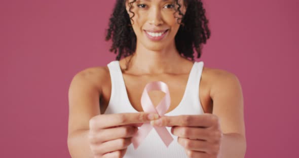Video of smiling biracial woman holding pink breast cancer ribbon alt