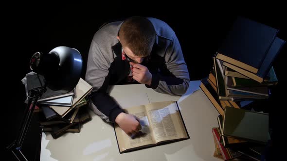 Man Leafing Through the Book and Falls Asleep. Black Background. View From Above alt