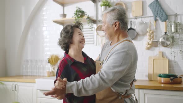 Asian mature senior couple is dancing and smiling in kitchen at home.