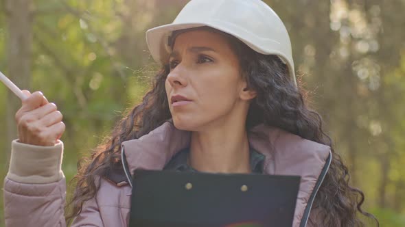 Female Technician Walking Taking Notes on Clipboard Notepad Paper in Park During Logging alt