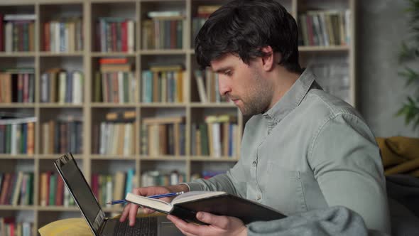 Portrait of a Man Sitting on a Sofa with a Laptop on the Background of a Bookshelf alt