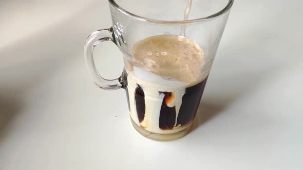 Making an Irish coffee. Transparent glass filled half way with black coffee and cream recently poure alt
