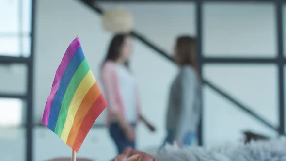 Close-up of LGBT Rainbow Flag with Blurred Lesbian Couple Hugging at the Background. Concept of alt