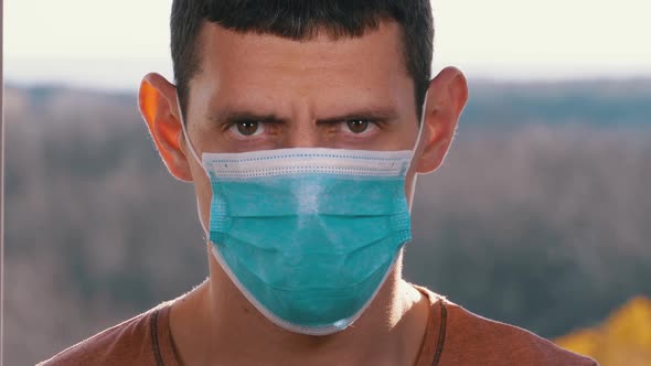 Young Man in a Medical Protective Face Mask Looking at the Camera on the Street Background alt