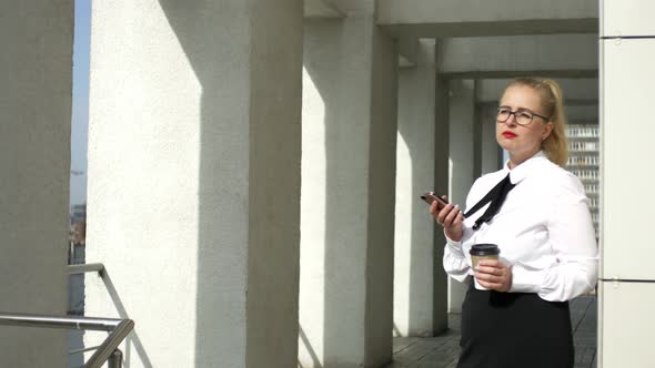 business woman with a smartphone is drinking coffee in the street