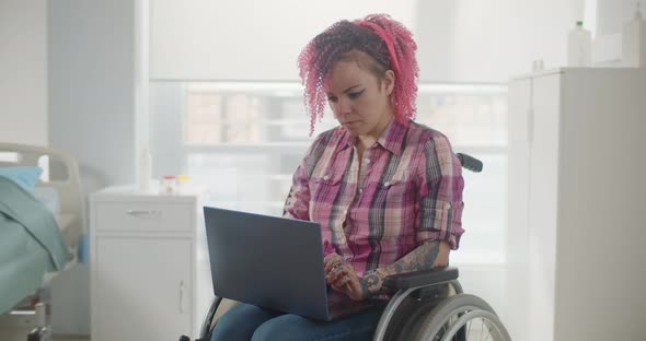 Disabled Woman Sitting in Wheelchair and Using Laptop in Hospital Ward alt