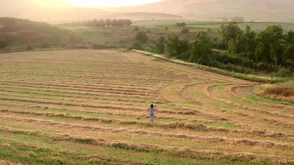 Girl Watches the Sunset on the Agricultural Field with Harvested Wheats alt