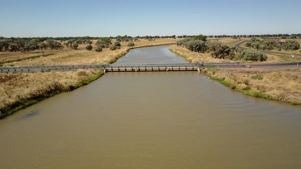 Aerial view of a bridge over a wide, murky river. The camera flies over and past. alt