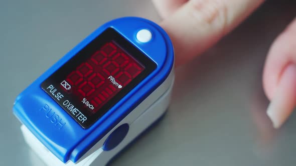 A Woman Inserts Her Finger Into a Medical Device to Measure Oxygen in the Blood alt