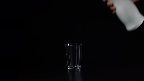 The Hand Pours Milk or Kefir From a Plastic White Bottle on a Black Background Into a Glass Glass