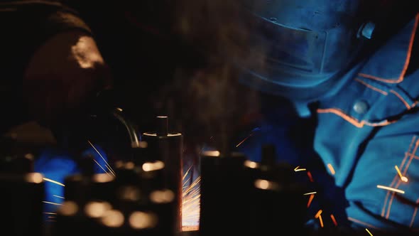 A Welder in a Protective Helmet and Clothes Welds Metal Sparks Illuminate It alt