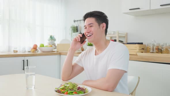 Asian handsome man talk on mobile phone call stand in kitchen at home. alt