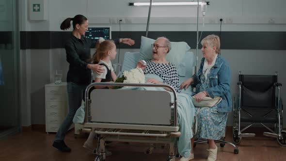 Senior Man Receiving Visit From Mother and Little Girl in Hospital Ward alt