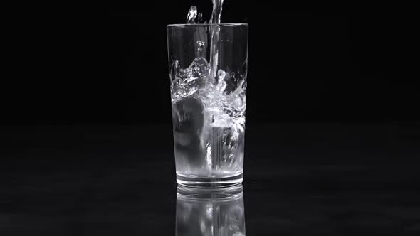 Water Pours into a Glass with Splashes on a Black Background