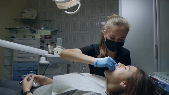 A Young Woman Dentist in a Mask and Medical Gloves Works with a Patient in a Dental Office