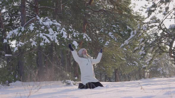 Happy Cute Girl in Warm Winter Clothes Sits in Snow Has Fun Throws It Up and Laughs Happily alt
