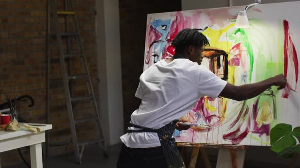Rear view of african american male artist wearing apron painting on canvas at art studio alt