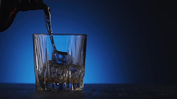 Whiskey Poured in Glass From Bottle at Blue Background with Copyspace at Right alt