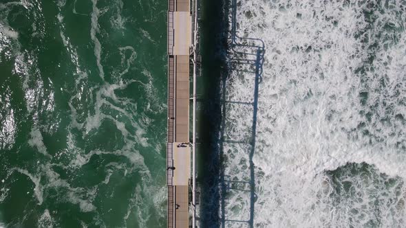Large waves breaking under a government infrastructure open to the public to use as a walk platform alt