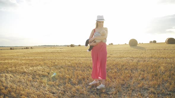 Mother Feeds the Baby Son with Breast in Haystack Field on Horizon with Sunlight alt