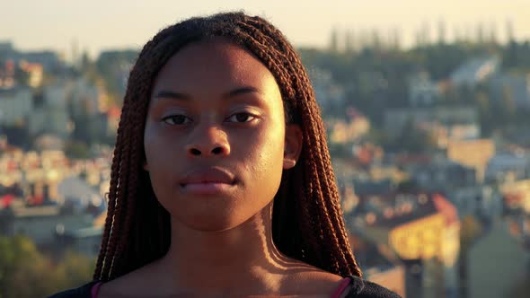 Young Black Woman Looks To Camera with Serious Face - City in Background alt