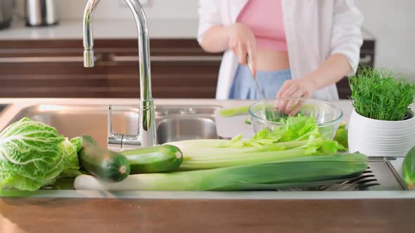 Female Prepares a Salad in the Kitchen Cuts Herbs and Green Vegetables to Make a Healthy Salad alt