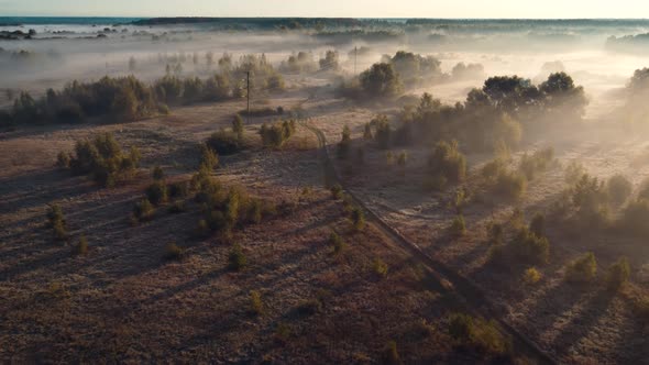 Flying over a road and a power line in the valley covered in fog