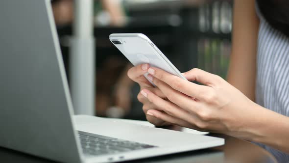 Close up young Asian woman using smartphone and laptop in cafe.