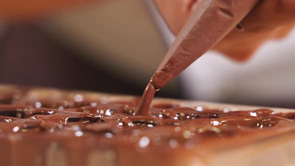 Chocolatier squeezing chocolate into praline mold, handmade fine chocolate praline production, close alt