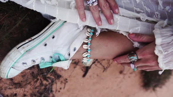 Closeup view of female hands as they run over white shoes, sitting on the grass and wearing a white alt