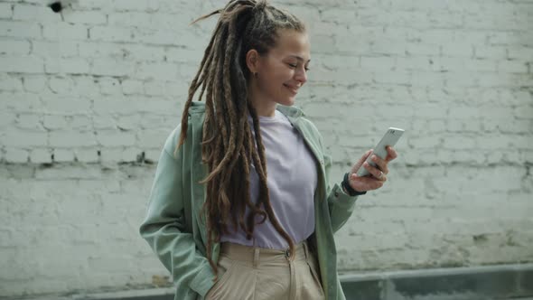 Portrait of Beautiful Young Woman with Dreadlocks Using Smartphone Texting Standing Outside alt