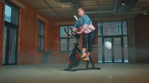 Healthy Caucasian Woman Exercising Workout on Stationary Cycling Machine Bike in Gym Slow Motion alt