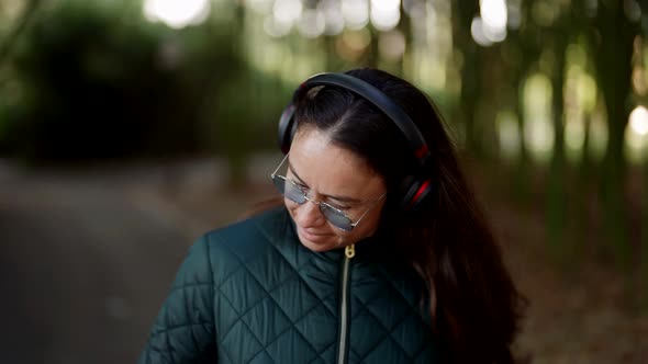 Charming Middleaged Woman is Enjoying Music By Headphones Walking in Park alt