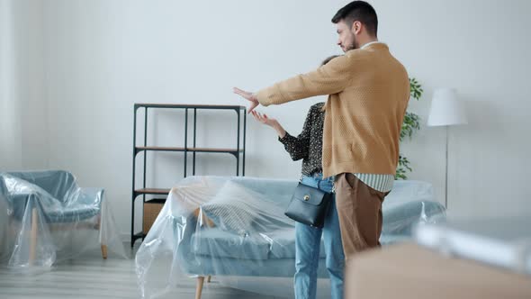 Young Family Man and Woman Discussing New Apartment Standing Indoors Talking and Gesturing alt