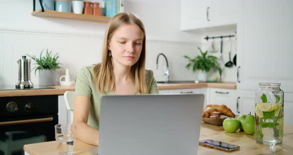 Young Woman or Female Student Works on Laptop at Home in Kitchen in Morning
