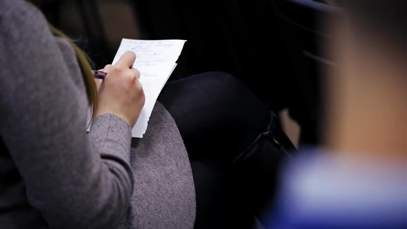 Young woman writes down information on a shirt of paper during conference. alt