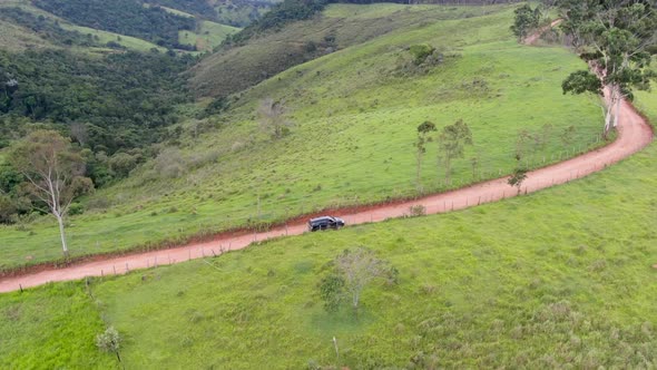 Aerial View of Car Driving Throuh a Small Dirt Road in the Middle of Green Tropical Valley. alt