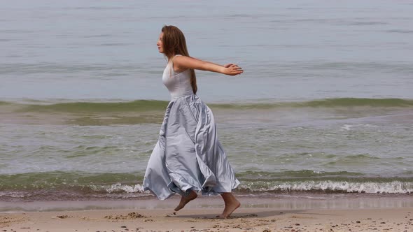 Attractive Young Woman in a Long Dress Dancing on The Beach 