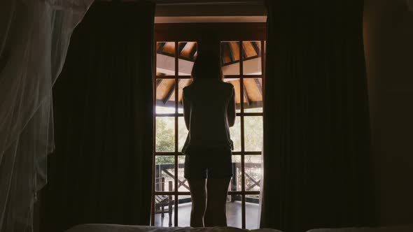 Back View Happy Young Tourist Woman Opening Chalet Curtains and Window Door, Walking Out To Stretch alt
