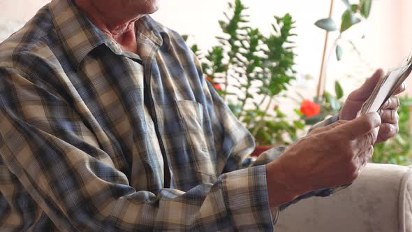 senior citizen looks at family photos while sitting in front of him on the couch at home. an elderly alt