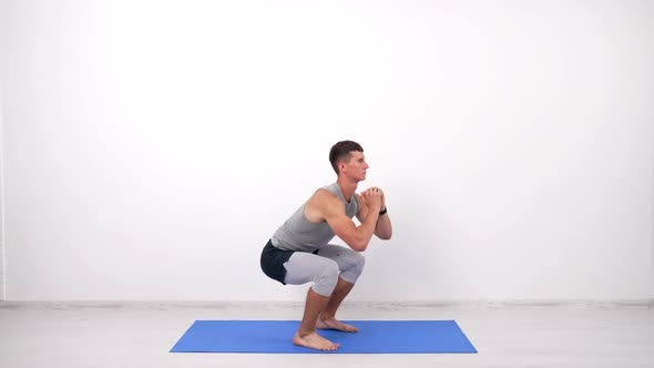 Concentrated Guy Doing Squats Exercise on Fitness Mat White Background Sport Training alt