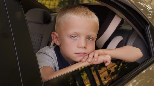 Portrait of a Sad Boy in the Car in the Back Seat He Leans on the Open Window alt