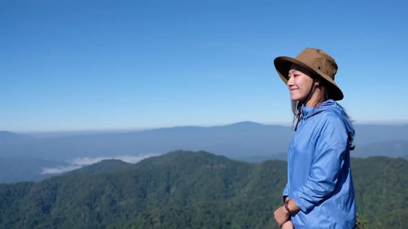 Slow motion of a female traveler standing on mountain peak, looking at a beautiful view