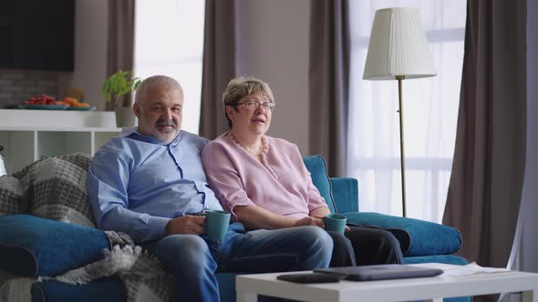 Happy Grandfather and Grandmother are Sitting Together at Living Room and Drinking Tea Grey Haired alt