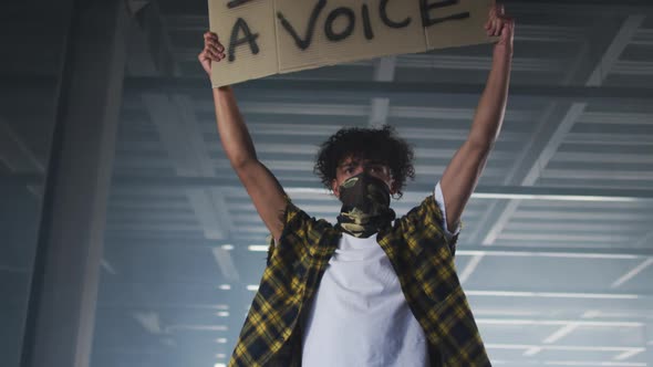Mixed race man wearing face mask holding protest placard in empty parking garage alt