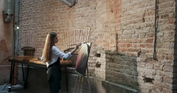 Backside View of Talented Innovative Pretty Female Artist Draws with Brush on the Canvas