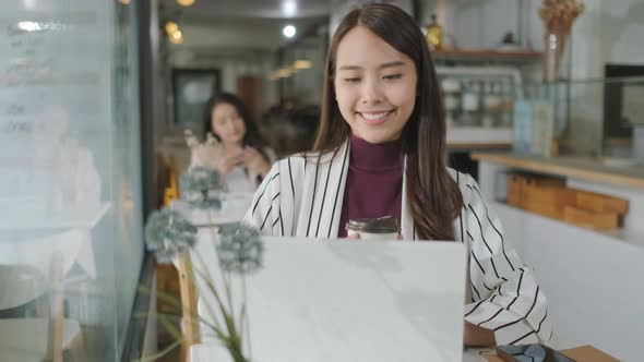 Asian woman using laptop in restaurant and looking outside dreaming about something
