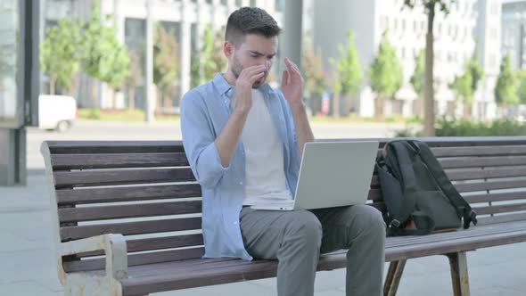 Young Man with Headache Using Laptop While Sitting on Bench alt
